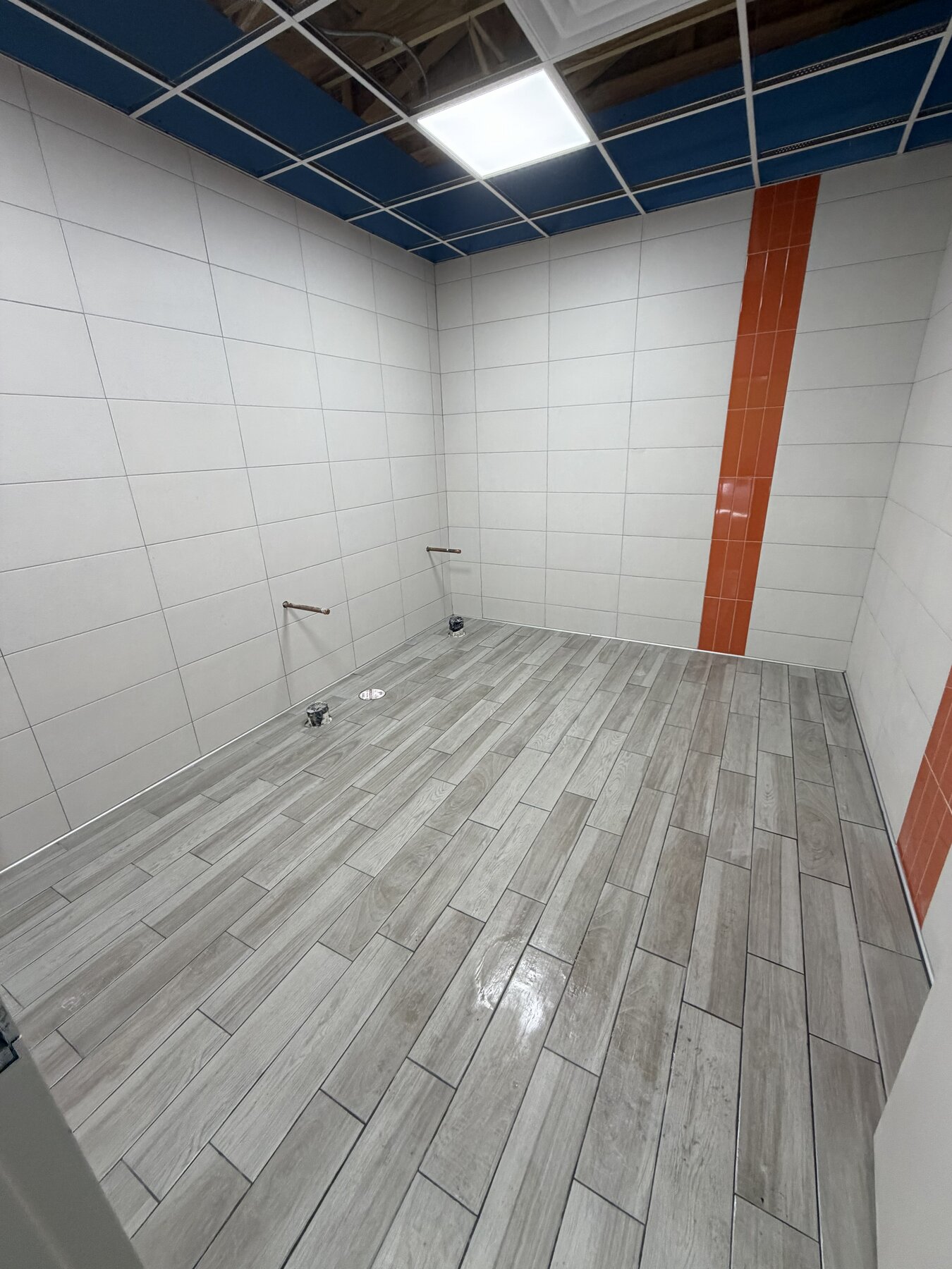 Commercial gas station restroom tile installation in Oklahoma — white wall tile, orange accent stripe, wood-look plank floor